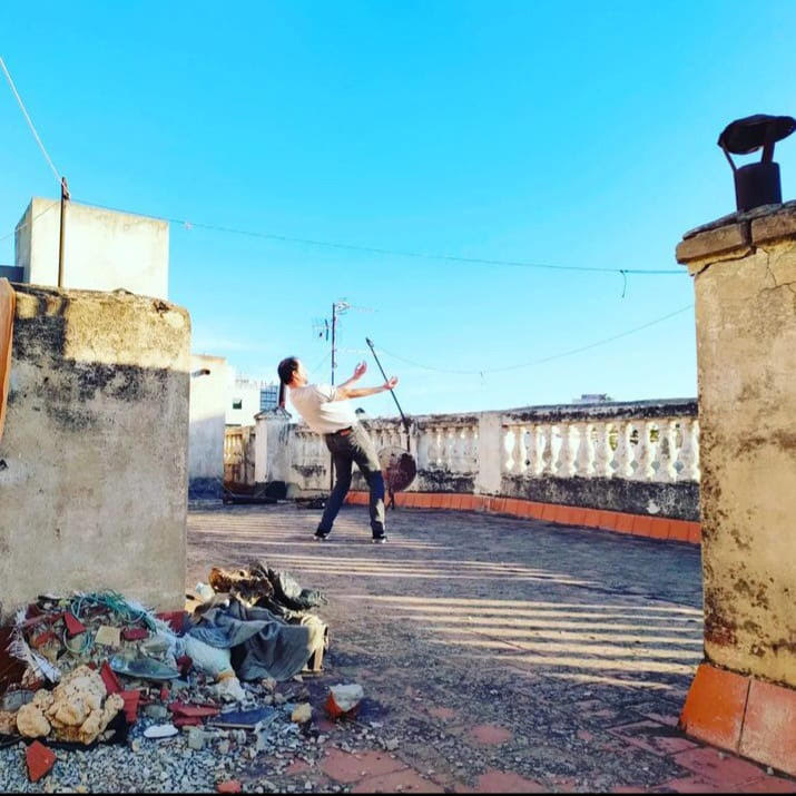 Danseur courbé vers l'arrière dans un décor de ville ensoleillée avec au premier plan des gravats.