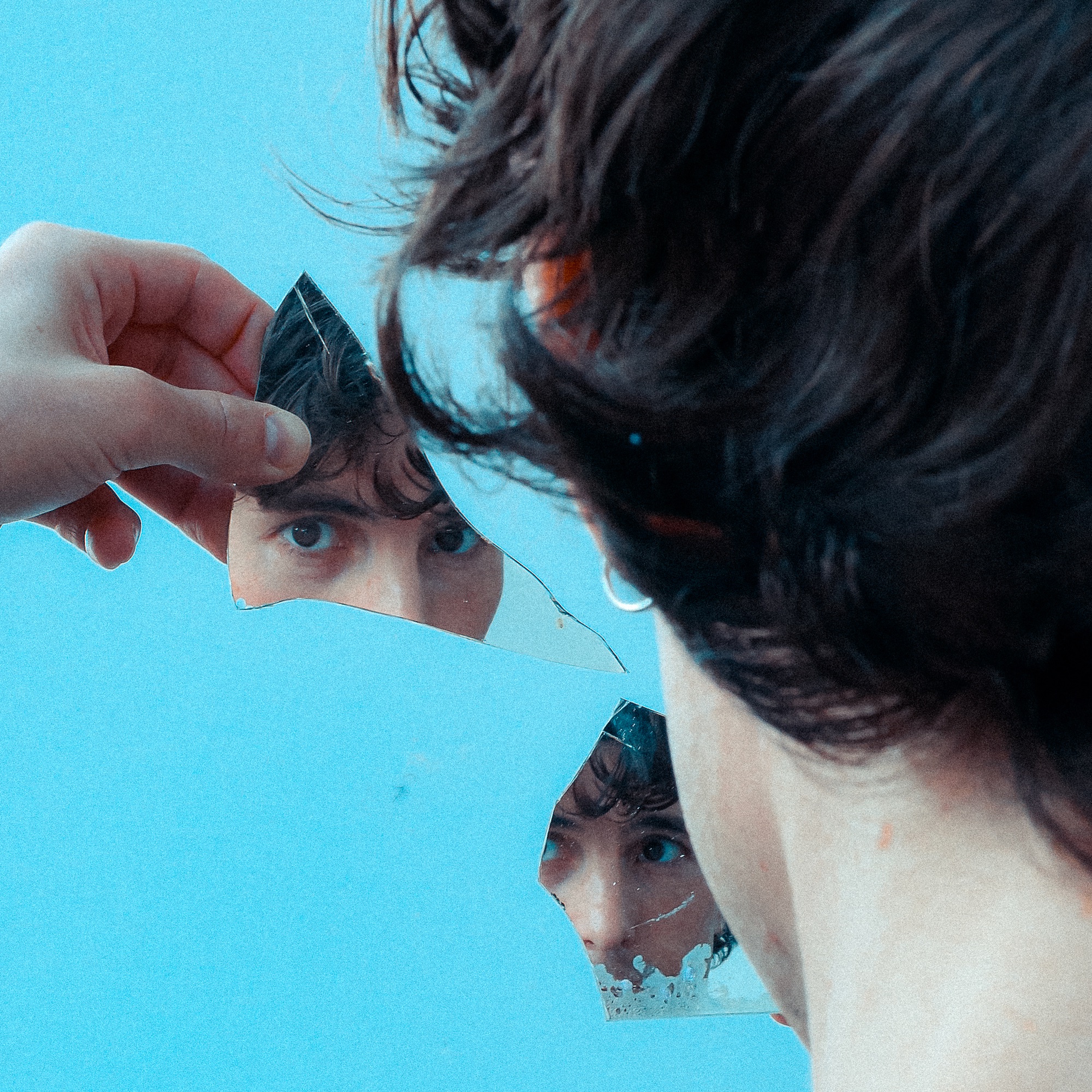 Un homme de dos se regarde dans deux fragments d'un miroir.
