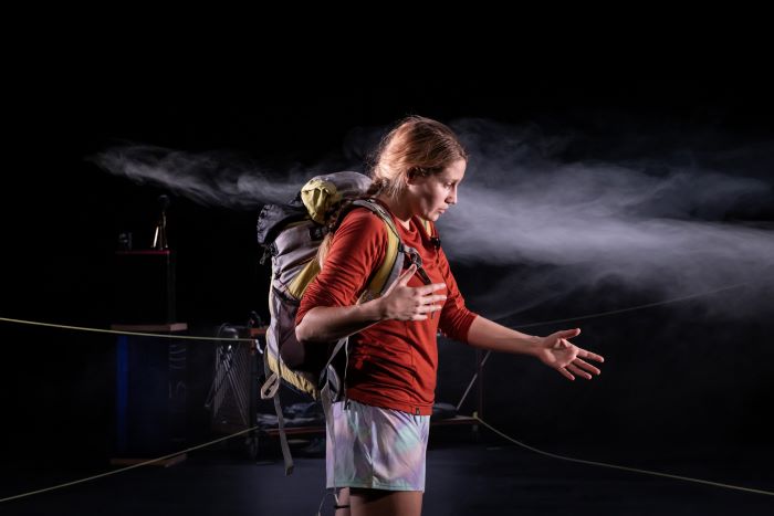 Une femme de profil portant un sac à dos de randonnée tend le bras gauche devant elle.